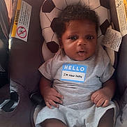 Jace is registered to the contest to win money with this photo: baby, infant, car_seat, soccer_ball_pattern, clothing, gray_outfit, curly_hair, cute, newborn, child, indoor, portrait, sitting, smiling, person, young_child, soft_lighting, human, headrest, feet