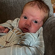 Beau is registered to the contest to win money with this photo: baby, infant, face, eyes, clothing, onesie, striped, lion_design, couch, furniture, indoors, soft, cozy, person, child, portrait, young, cute, expression, relaxed