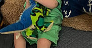 Christopher is registered to the contest to win money with this photo: baby, child, infant, plush_toy, green_clothing, socks, blanket, cushion, quilted_surface, indoors, cute, chewing, seated, soft_toy, comfort, portrait, playful, happy, young, cozy