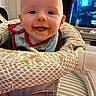 baby, child, messy_face, high_chair, indoor, smiling, food_stains, bib, seat, person, cute, happy, infant, face, head, clothing, home, television, background, furniture