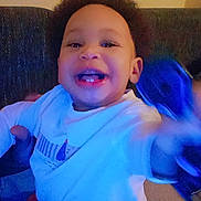 Nissam a rejoint le concours — aidez-le/la à gagner de superbes lots ! child, toddler, smile, teeth, afro, curly_hair, shirt, sitting, couch, indoors, portrait, happy, hand, arm, blurry_motion, toy, blue_tone, evening, baby, person