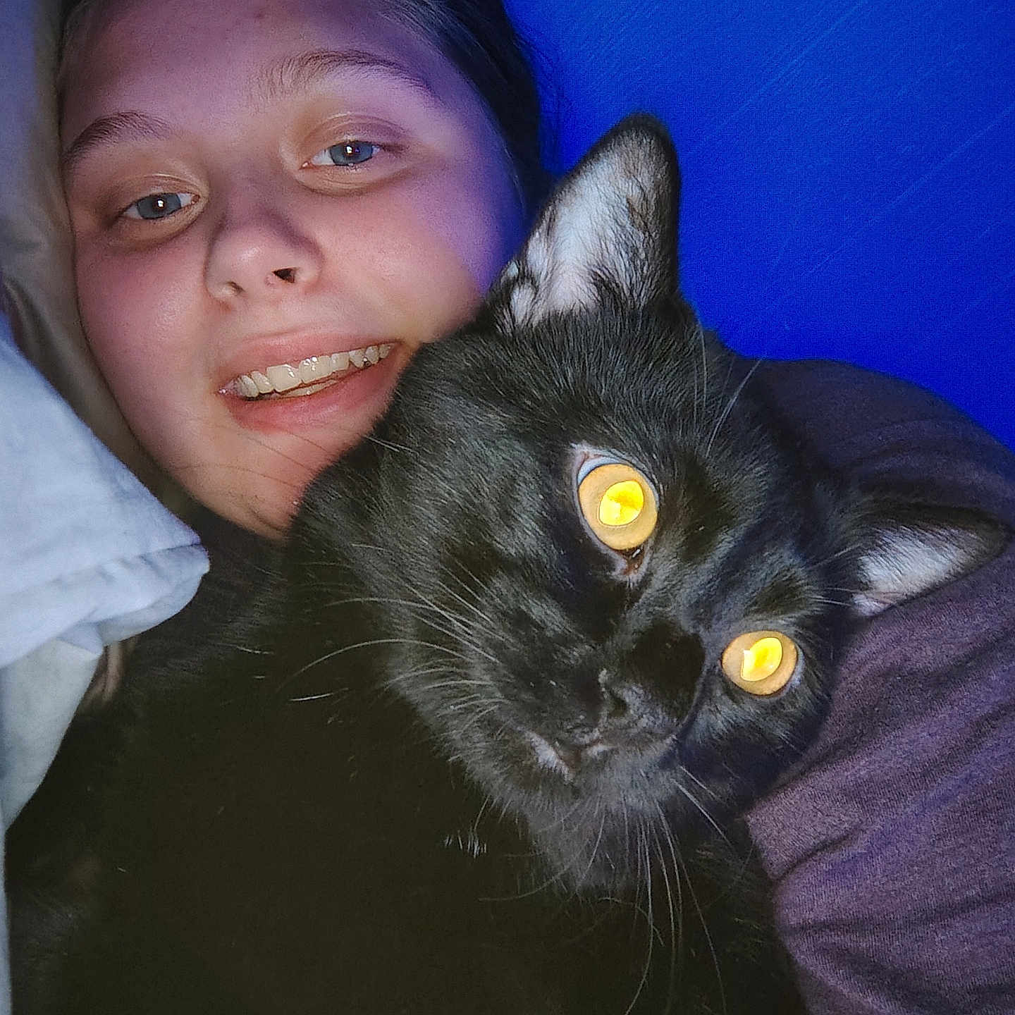 Lucky is registered to the contest to win money with this photo: animal, black_cat, blue_background, cat, closeup, companion, cozy, cute, face, feline, glowing_eyes, happy, human, indoor, person, pet, portrait, smiling, snuggling, warm