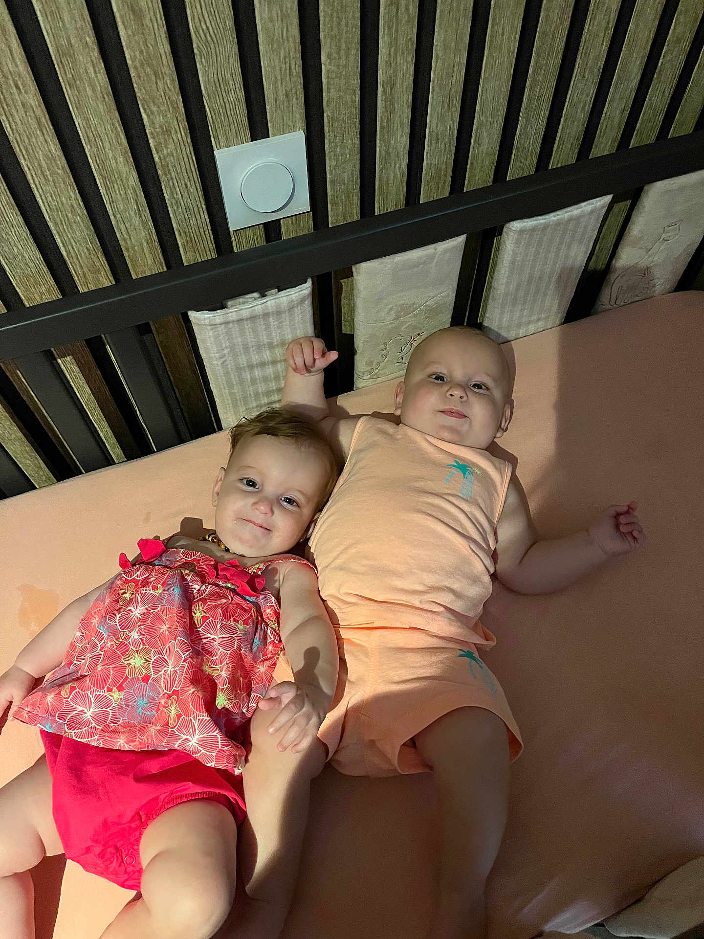 Noé participe au concours pour gagner de l'argent avec cette photo : baby, babies, child, infant, bed, holding_hands, clothing, floral, pink, peach, crib, sleeping_area, cute, smiling, indoor, person, toddler, happy, skin, head