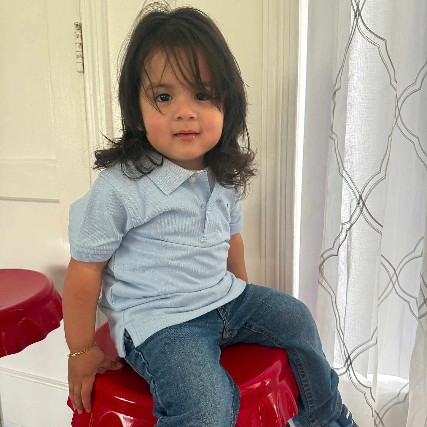 Orlando is registered to the contest to win money with this photo: child, toddler, portrait, sitting, smiling, face, long_hair, blue_shirt, jeans, sneakers, red_stool, indoors, home, curtains, door, window, natural_light, fashion, happy, photography