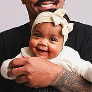 Ashley participe au concours pour gagner de l'argent avec cette photo : baby, infant, headband, bow, smiling, tattoo, adult, holding, hands, portrait, closeup, cute, happy, person, skin, face, clothing, black_shirt, studio, background