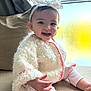 baby, child, smiling, headband, bow, white_jacket, pink_trim, couch, window, natural_light, indoors, cute, happy, portrait, infant, sitting, cozy, warm_clothing, person, face