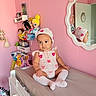 Melanie is registered to the contest to win money with this photo: baby, child, pink_wall, mirror, changing_table, crocheted_outfit, bonnet, dolls, princess_dolls, clothing, socks, furniture, room, reflection, toy, sitting, cute, indoor, decor, childrens_room