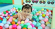 Melanie joined the competition — help win amazing prizes! toddler, child, ball_pit, colorful_balls, pink_bows, play_area, indoor, educational_toys, happy, cute, playful, person, young_child, smiling, hair_bows, pastel_colors, toys, developmental_toys, crawling, fun
