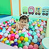 toddler, child, ball_pit, colorful_balls, pink_bows, play_area, indoor, educational_toys, happy, cute, playful, person, young_child, smiling, hair_bows, pastel_colors, toys, developmental_toys, crawling, fun