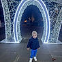 Freddie is registered to the contest to win money with this photo: child, boy, smiling, jacket, sneakers, pants, night, lights, arch, outdoor, pavement, festive, holiday, decoration, people, urban, street, happy, cute, clothing