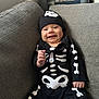baby, smiling, costume, skeleton, hat, black_clothing, couch, gray, infant, indoors, happy, cute, child, portrait, seated, clothing, small_hand, face, young, cozy
