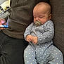 baby, infant, sleeping, pacifier, onesie, blue_clothing, stars_pattern, couch, sofa, adult, hoodie, phone, hand, indoor, relaxation, comfort, face, person, casual, seated