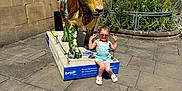 Aria joined the competition — help win amazing prizes! child, girl, statue, lion, sunglasses, outdoor, building, sidewalk, plants, flowers, sunny, daytime, casual_clothing, playful, peace_sign, concrete, urban, flowerbed, bench, sculpture