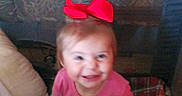 Rosalie joined the competition — help win amazing prizes! toddler, child, red_bow, pink_shirt, plaid_blanket, smiling, indoor, couch, pillow, baby, cute, sitting, happy, playful, young_child, home, person, face, head, blanket