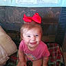 toddler, child, red_bow, pink_shirt, plaid_blanket, smiling, indoor, couch, pillow, baby, cute, sitting, happy, playful, young_child, home, person, face, head, blanket