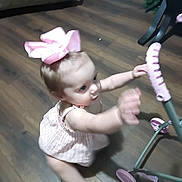 Rosalie is registered to the contest to win money with this photo: toddler, child, baby, pink_bow, toy, stroller, wooden_floor, indoor, playful, reaching, motion_blur, dress, cute, young_child, person, flooring, home, small_child, exploration, infant