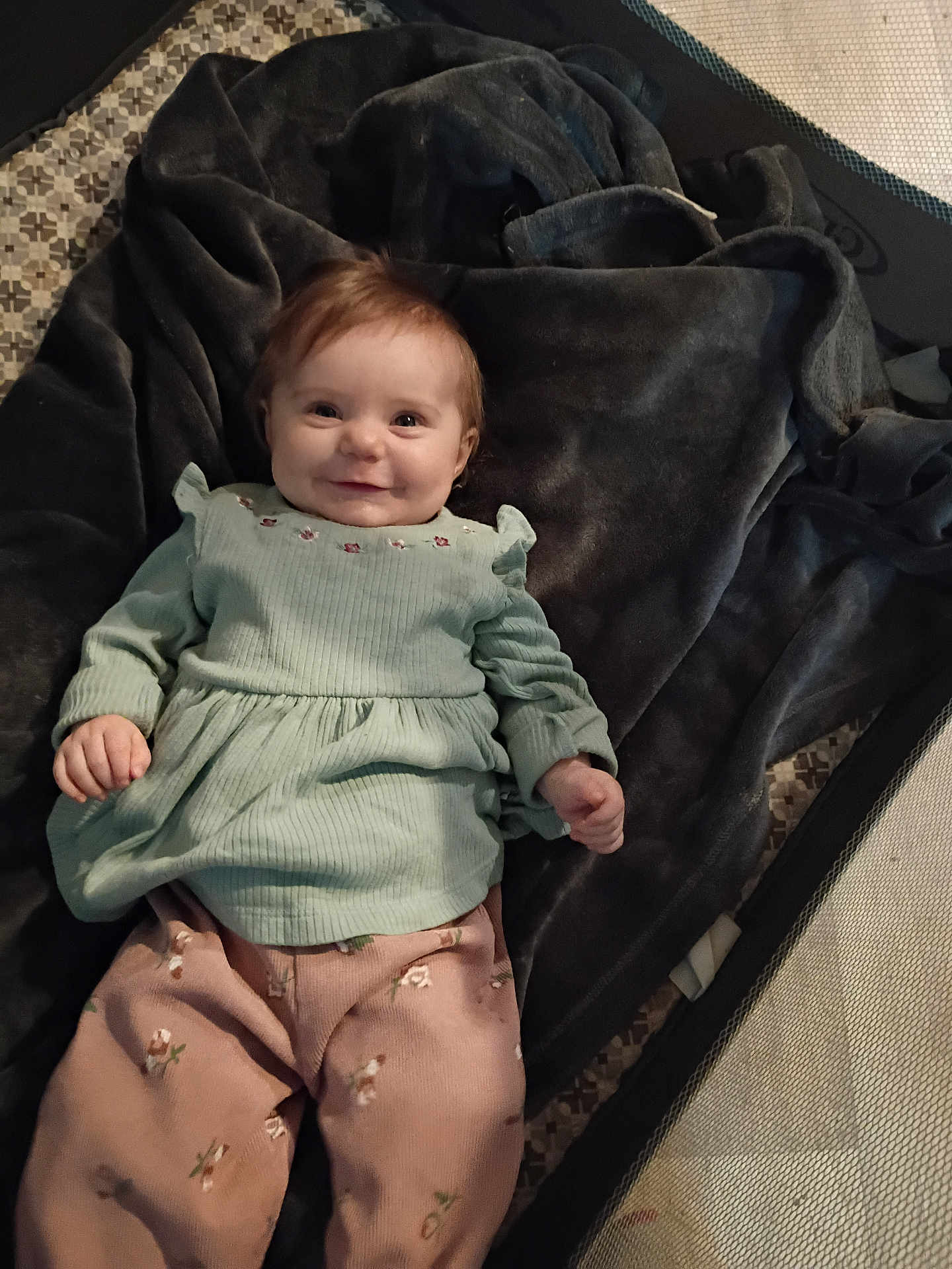 Rosalie joined the competition — help win amazing prizes! baby, child, smile, face, clothing, blanket, playpen, infant, person, pink_pants, green_top, happy, cute, indoor, soft_texture, portrait, young_child, lying_down, cozy, comfort