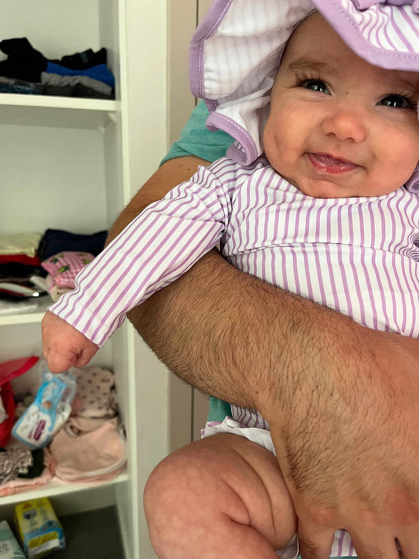 Sofia a rejoint le concours — aidez-le/la à gagner de superbes lots ! baby, infant, smile, striped_clothing, hat, arm, adult, holding, shelf, clothes, baby_supplies, diapers, indoor, happy, cute, person, skin, flesh, close_up, portrait