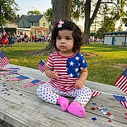 Kshaira joined the competition — help win amazing prizes! toddler, child, curly_hair, pink_bow, american_flag, patriotic_clothing, stars_and_stripes, picnic_table, confetti, outdoor, park, grass, tree, people, daylight, casual, sitting, celebration, event, cute