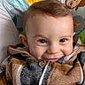 animal_pattern, baby, buttoned_clothing, cheeky_grin, child, closeup, colorful_background, cozy, cute, eyes, face, happy, indoor, infant, plaid_jacket, playful, portrait, smile, warm_clothing, young_child