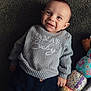 baby, smiling, sweater, clothing, carpet, toy, colorful, soft_toy, child, cute, portrait, indoor, happy, person, infant, face, hand, button, pattern, cozy