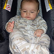 Noah is registered to the contest to win money with this photo: baby, infant, car_seat, pajamas, child, sleepy, hands, face, cute, indoor, seat, warning_label, patterned_clothing, young_child, soft_lighting, exploring, close_up, cozy, infant_clothing, portrait