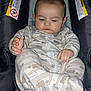 baby, infant, car_seat, pajamas, child, sleepy, hands, face, cute, indoor, seat, warning_label, patterned_clothing, young_child, soft_lighting, exploring, close_up, cozy, infant_clothing, portrait