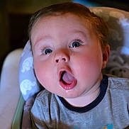 Bailey joined the competition — help win amazing prizes! baby, child, high_chair, toy, surprised_expression, face, blue_eyes, gray_shirt, monkey_design, indoor, closeup, infant, cute, person, mouth_open, cheeks, soft_lighting, seat, plastic_toy, colorful