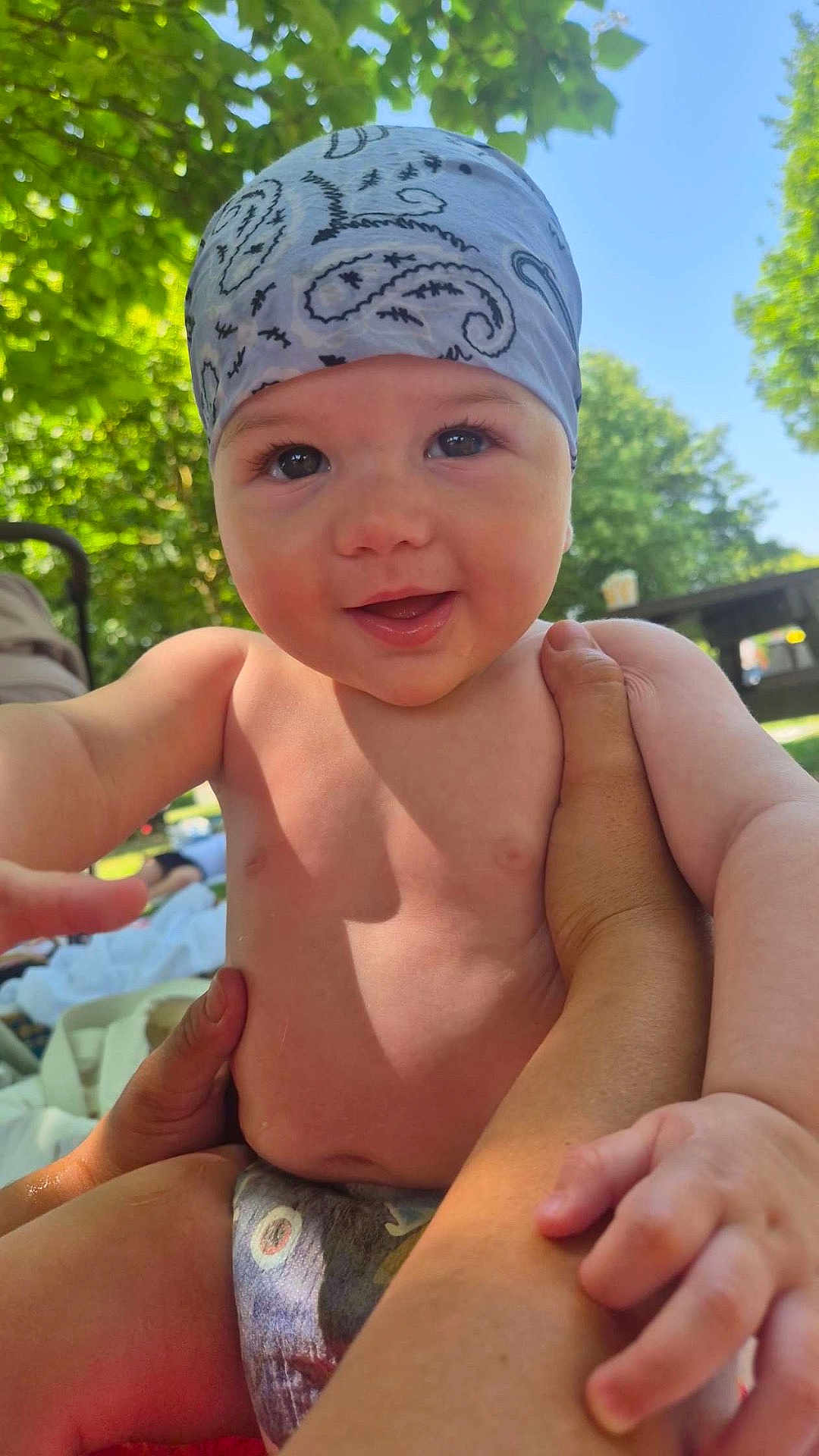 Charles a rejoint le concours — aidez-le/la à gagner de superbes lots ! baby, child, bandana, outdoor, smiling, happy, skin, hand, arm, nature, tree, sunlight, diaper, grass, person, summer, blue_sky, closeup, portrait, daylight
