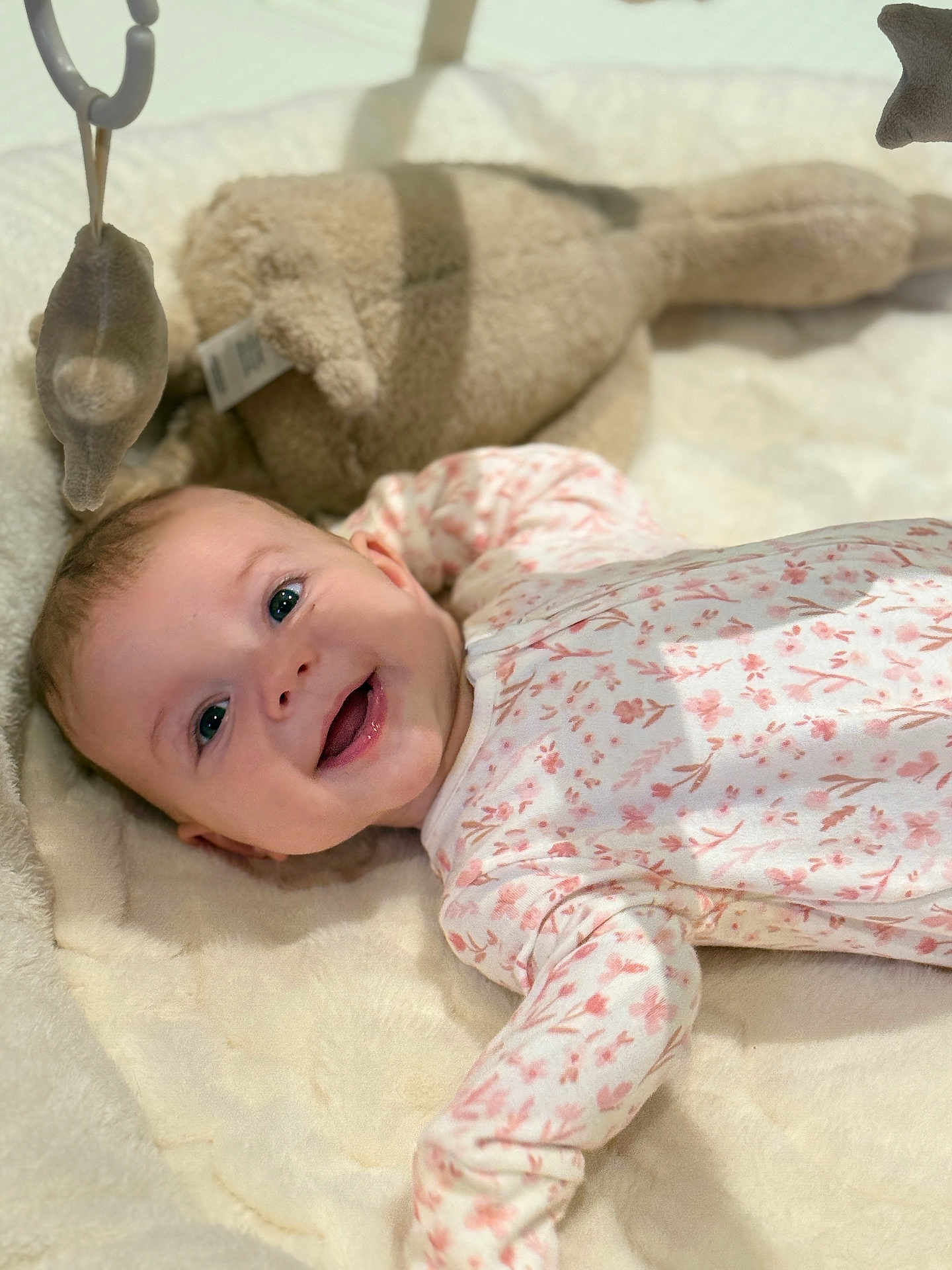 Ayana is registered to the contest to win money with this photo: baby, smiling, onesie, floral_pattern, plush_toy, blanket, infant, happy, face, lying_down, soft_toys, nursery, child, cute, indoors, playtime, cozy, head, person, young_child