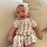 Ayana joined the competition — help win amazing prizes! baby, infant, smile, headband, bow, striped_clothing, romper, white_shirt, couch, soft_texture, indoor, happy, child, person, cute, sitting, small_hands, small_feet, comfortable, cozy