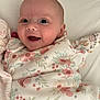 baby, smiling, infant, floral_pattern, blanket, happy, face, cute, lying_down, indoors, soft_texture, cozy, child, pajamas, newborn, person, skin, head, expression, sleepwear