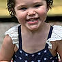 child, toddler, smiling, toy, guitar, red_bow, curly_hair, dress, stars_pattern, outdoor, blurred_background, happy, cute, person, young_child, holding, playful, summer_clothing, portrait, fun