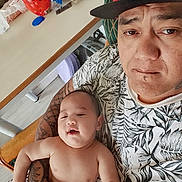 Wilson a rejoint le concours — aidez-le/la à gagner de superbes lots ! baby, cap, casual, chair, child, expression, face, furniture, hand, holding, home, indoor, man, person, relaxation, shirt, skin, smile, table, tattoo