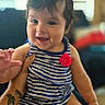 baby, child, infant, smiling, happy, portrait, sitting, striped_outfit, red_flower, indoors, family, adult, lap, tattoo, hands, face, hair, couch, window, natural_light