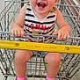 toddler, child, shopping_cart, smile, happy, curly_hair, clothing, shoes, socks, grocery_store, aisle, metal, floor, person, retail, store, shopping, baby, young_child, cute