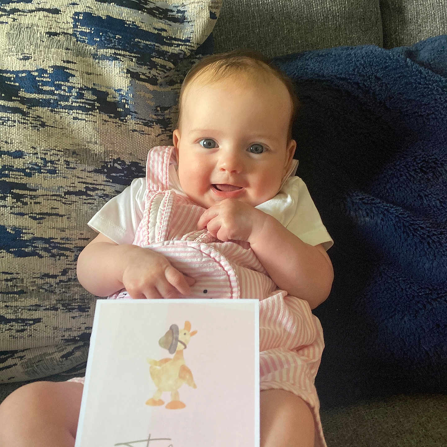 Rose is registered to the contest to win money with this photo: baby, blanket, child, clothing, couch, cute, eyes, face, hand, happy, indoor, infant, milestone_card, person, pillow, pink, sitting, smile, striped, white