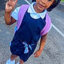 Miss Naomi is registered to the contest to win money with this photo: child, girl, pony_tail, hair_accessories, peace_sign, backpack, dress, white_shirt, socks, sneakers, outdoor, pavement, grass, building, smiling, standing, young, cute, fashion, happy