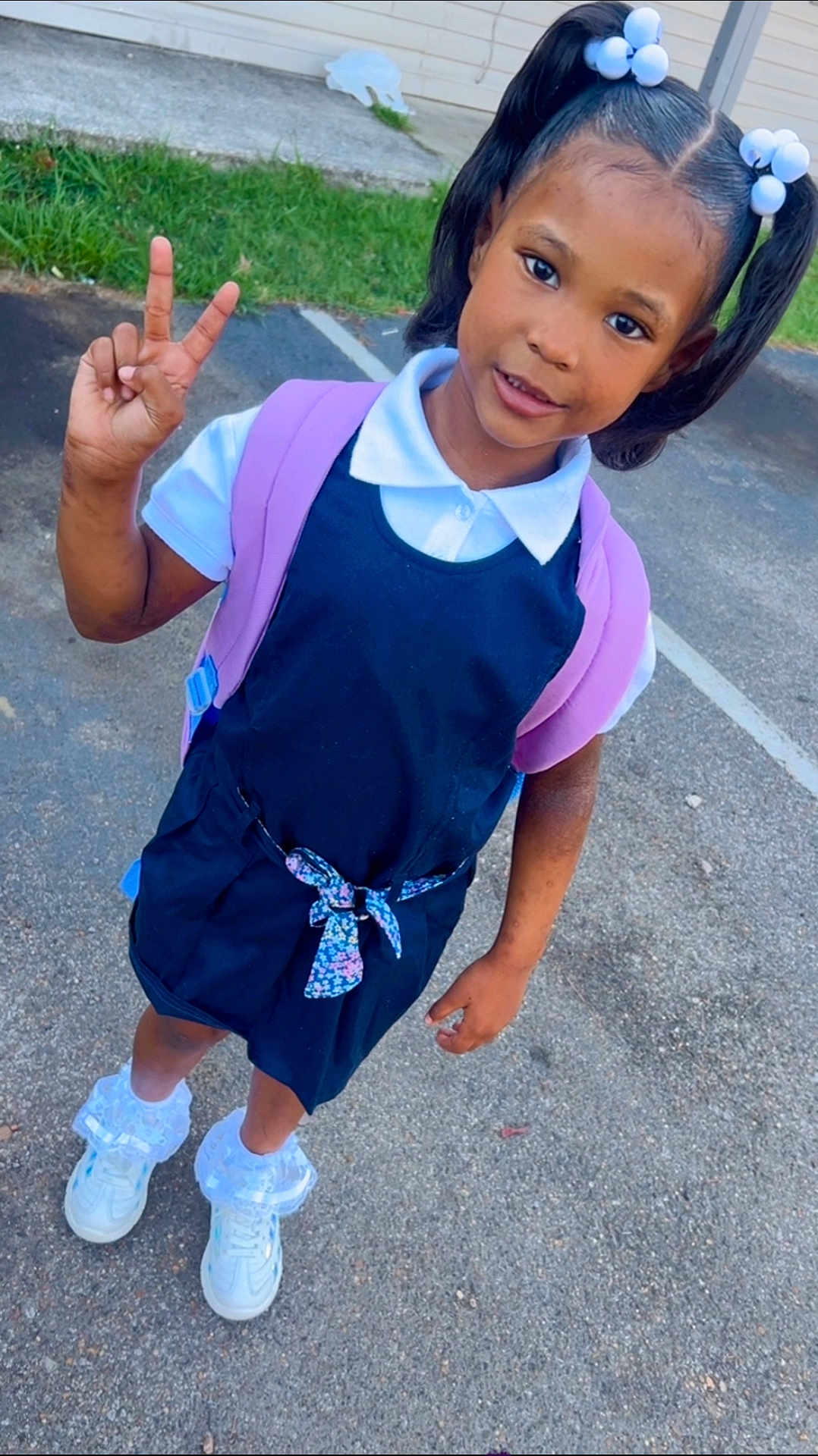 Miss Naomi is registered to the contest to win money with this photo: child, girl, pony_tail, hair_accessories, peace_sign, backpack, dress, white_shirt, socks, sneakers, outdoor, pavement, grass, building, smiling, standing, young, cute, fashion, happy