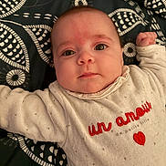 Luna participe au concours pour gagner de l'argent avec cette photo : baby, infant, face, eyes, clothing, white_outfit, patterned_blanket, lying_down, closeup, cute, child, portrait, red_text, heart, arms_outstretched, soft_fabric, indoors, skin, head, expression