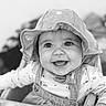 Luna participe au concours pour gagner de l'argent avec cette photo : baby, black_and_white, child, closeup, clothing, cute, expression, face, happy, hat, headwear, indoor, infant, joy, overalls, person, portrait, sitting, smiling, young