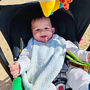 Maël participe au concours pour gagner de l'argent avec cette photo : baby, stroller, bib, white_clothing, plush_toy, smiling, joyful, child, infant, outdoor, sunlight, sand, seatbelt, toy, happy, person, portrait, baby_toy, infancy, cute