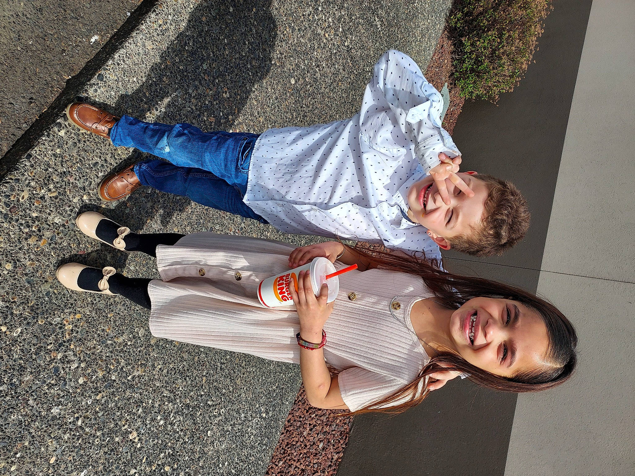 Nevaeh is registered to the contest to win money with this photo: asphalt, child, clothing, eyewear, fun, gesture, happy, human_leg, joy, knee, leg, leisure, person, road_surface, shadow, sidewalk, sitting, smile, sneakers, thigh