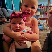 Knoxxlee joined the competition — help win amazing prizes! baby, child, sibling, hug, smile, headband, indoor, couch, family, happy, person, arm, hand, living_room, furniture, casual, warm_lighting, cute, portrait, toddler