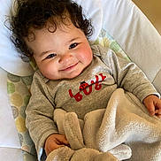 Kyla is registered to the contest to win money with this photo: baby, blanket, child, clothing, comfort, curly_hair, cushion, cute, face, happy, indoors, infant, person, playful, plush_toy, portrait, seat, smile, soft_texture, toddler