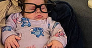 Aaliyah participe au concours pour gagner de l'argent avec cette photo : baby, sleeping, glasses, onesie, cartoon_characters, blanket, couch, child, indoors, cozy, hands, face, hair, soft, resting, peaceful, cute, portrait, relaxed, home