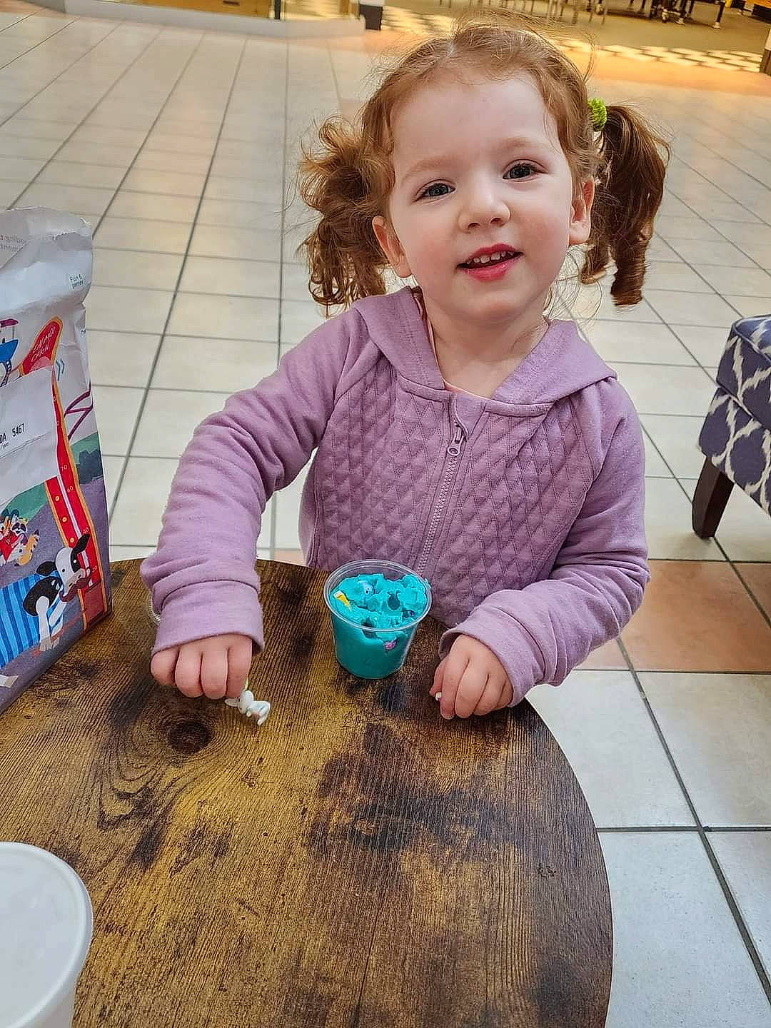 Rosemary is registered to the contest to win money with this photo: baby, baby_toddler_clothing, child, floor, flooring, fun, happy, hardwood, joy, leisure, pattern, person, play, sharing, sitting, smile, table, tableware, toddler, varnish