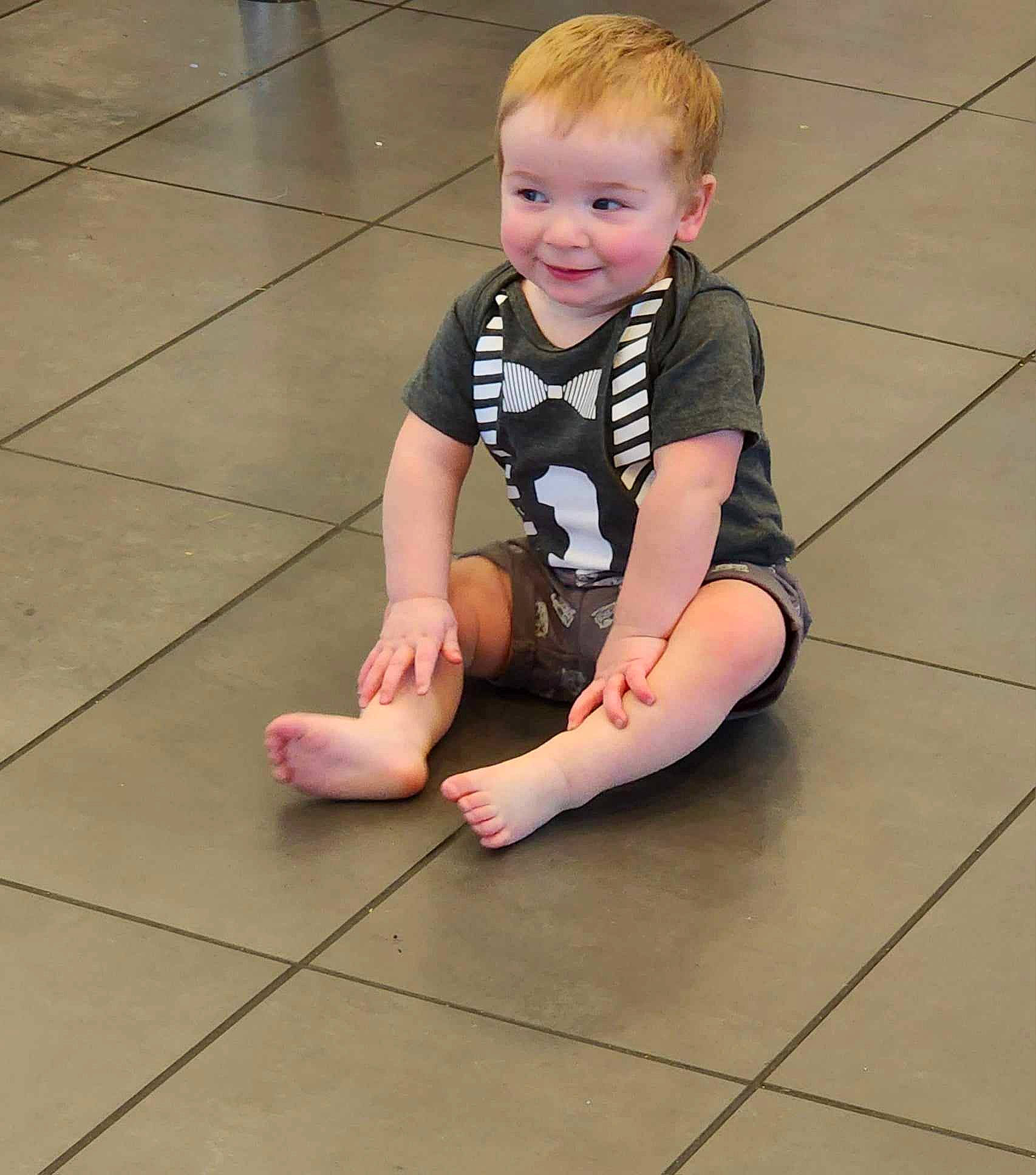 Enoch is registered to the contest to win money with this photo: baby_toddler_clothing, child, face, floor, flooring, foot, hardwood, head, human_body, human_leg, joint, joy, knee, leg, person, skin, sleeve, smile, sock, thigh
