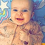 baby, smiling, blue_eyes, onesie, pink_clothing, dog_pattern, infant, happy, cute, lying_down, blanket, stars, cartoon, face, child, portrait, hand, fingers, indoors, closeup