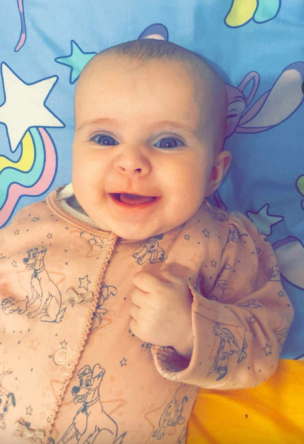 Antonia joined the competition — help win amazing prizes! baby, smiling, blue_eyes, onesie, pink_clothing, dog_pattern, infant, happy, cute, lying_down, blanket, stars, cartoon, face, child, portrait, hand, fingers, indoors, closeup
